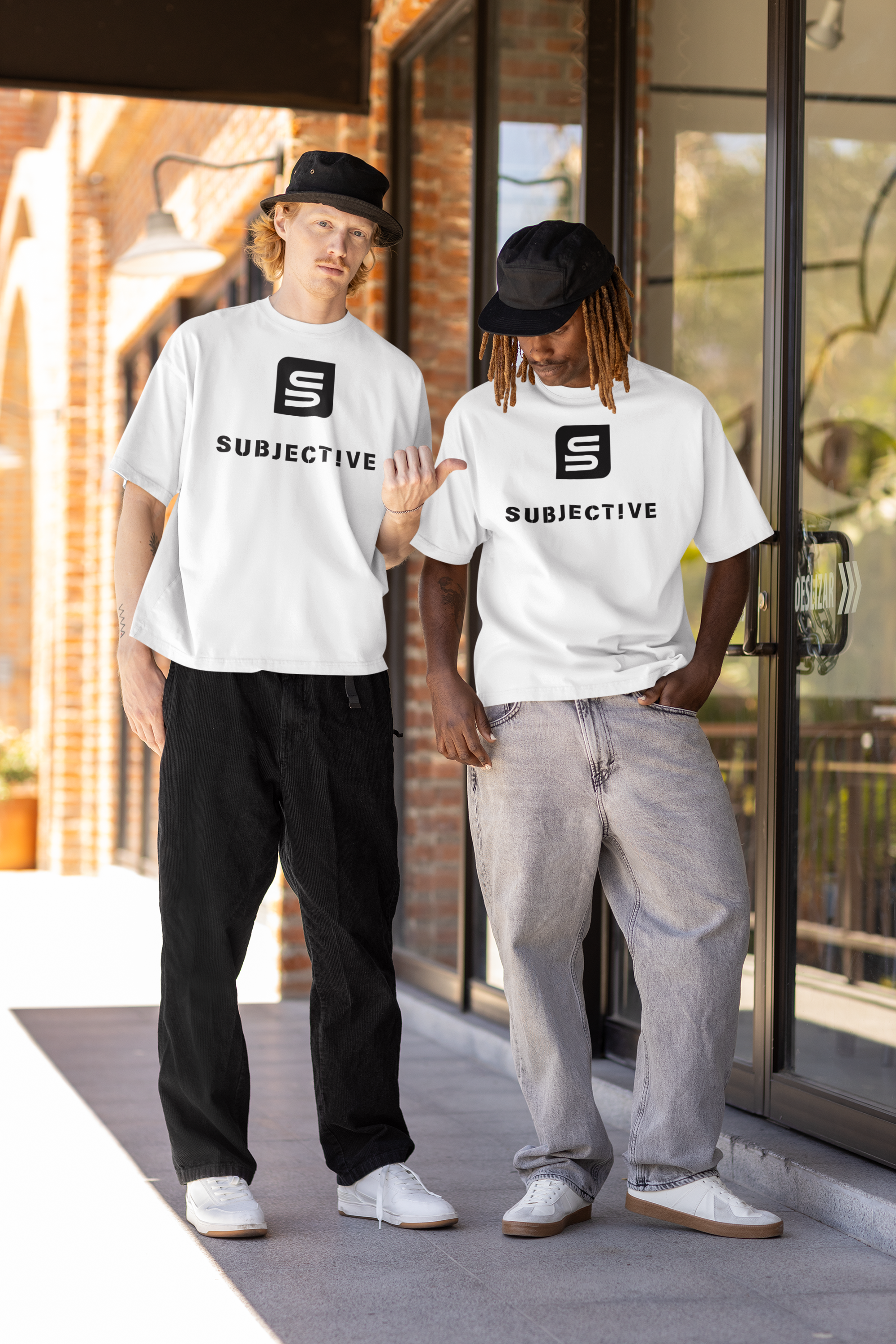 Two people wearing white 'Subjective' t-shirts standing outside a building.